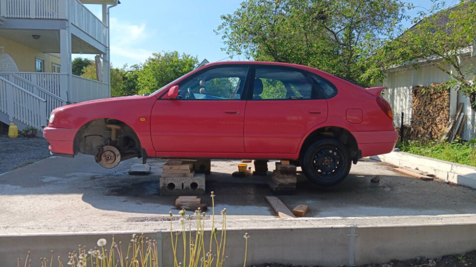 A red car with wheels removed resting on wooden blocks