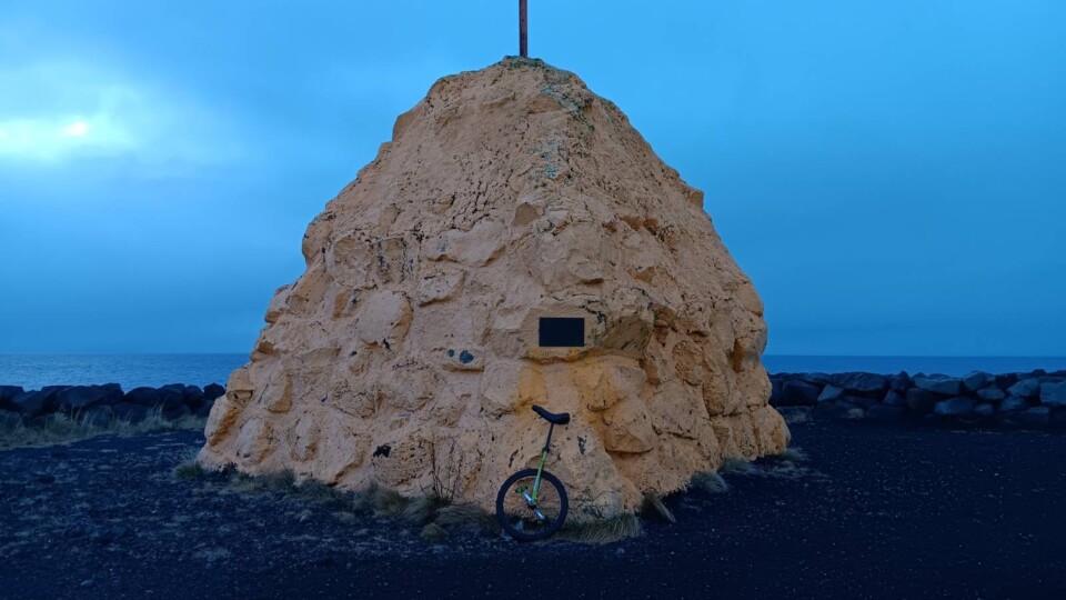 Unicycle in front of a large mound of stones and concrete painted yellow. In the background is a dark brooding, blue sky.