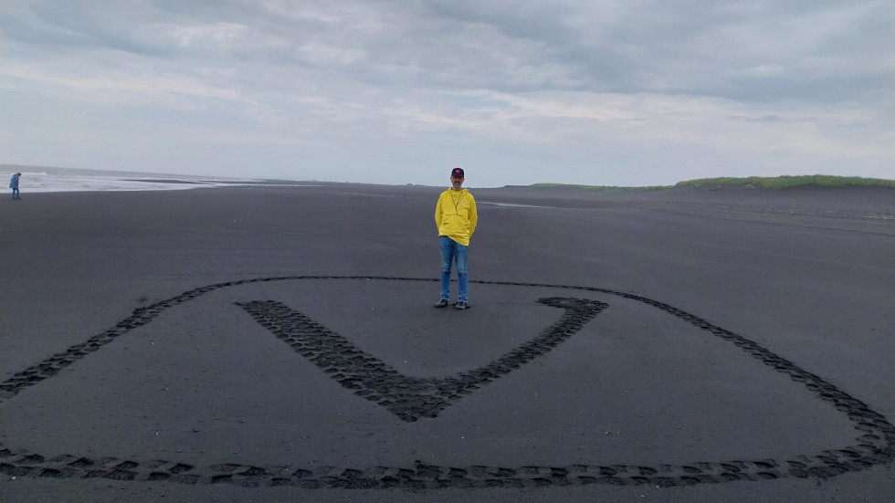 Man standing on black sand with a large Vivaldi logo crafted in that sand