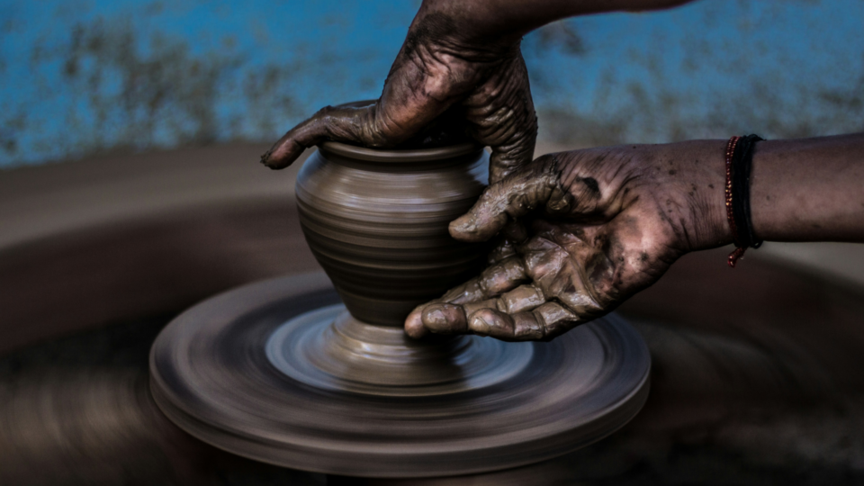 Hands molding a vase out of clay on a pottery wheel.