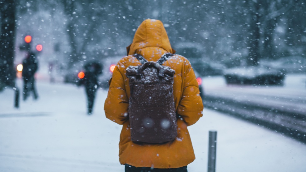 Man with back to photographer, wearing yellow jacket and backback in the snow