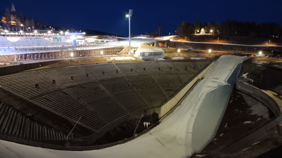 A view looking down at the bowl of the Holmenkollen ski jump at night time. The sky is dark but there is lots of lighting aorund. There is also snow inside the jump.