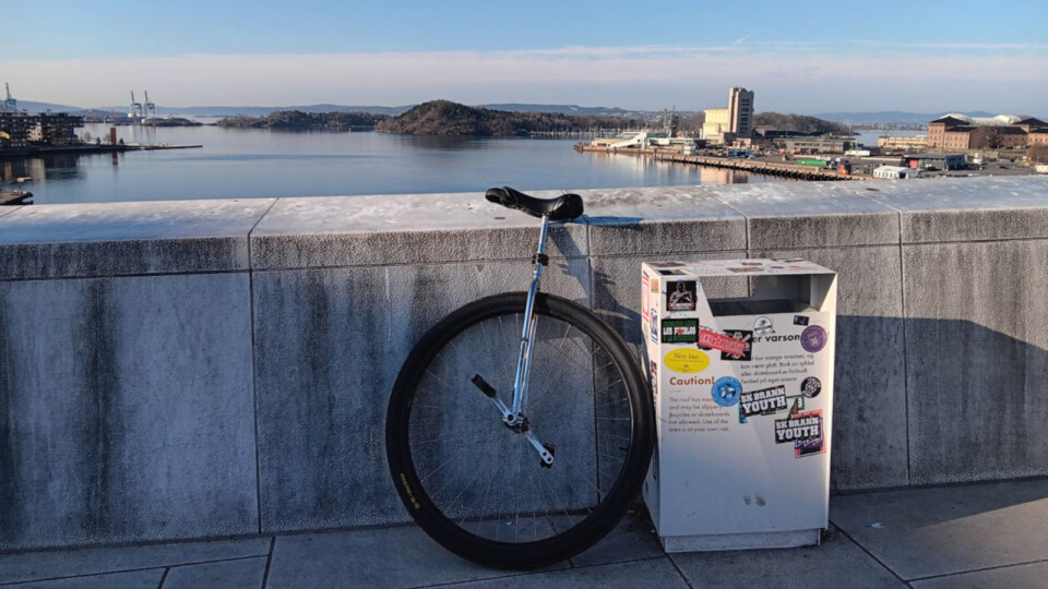A large wheeled unicycle leaning on a white stone wall before the Oslo fjord