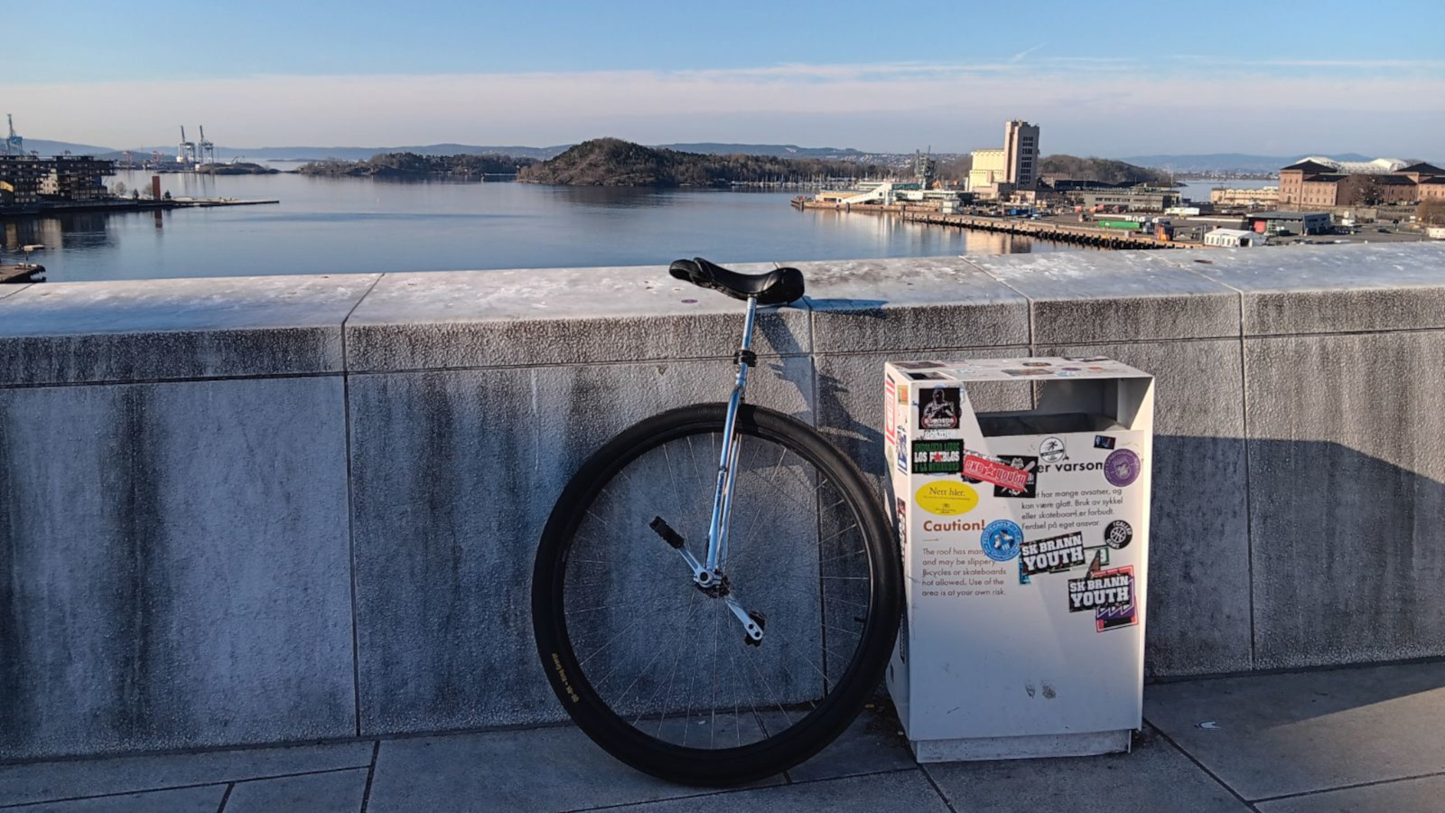 A large wheeled unicycle leaning on a white stone wall before the Oslo fjord