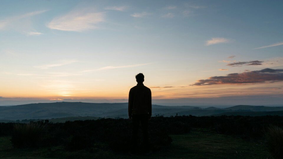 Man silhouetted, standing and looking at a sunset