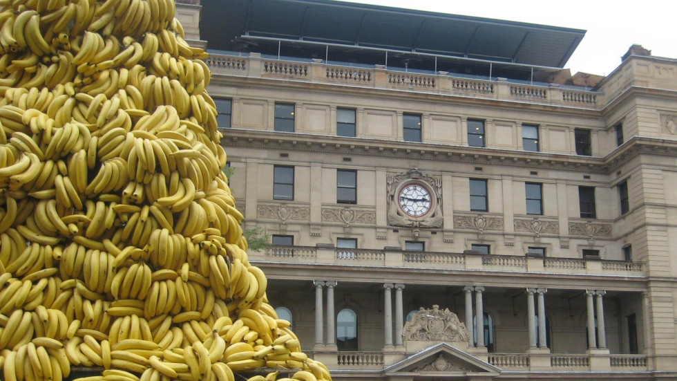 A large tower of bananas in front of a historic building with columns and a central clock. Taken in Sydney, 2010.